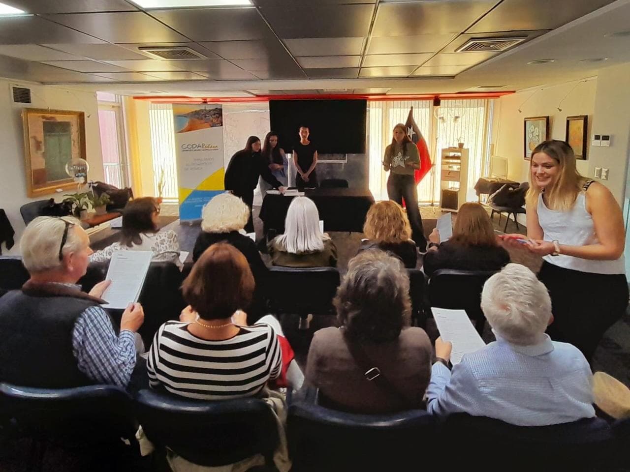 Participantes sentados en la sala, con una hoja en la mano, mientras el equipo de estudiantes de la UAI dirige la actividad desde el frente.